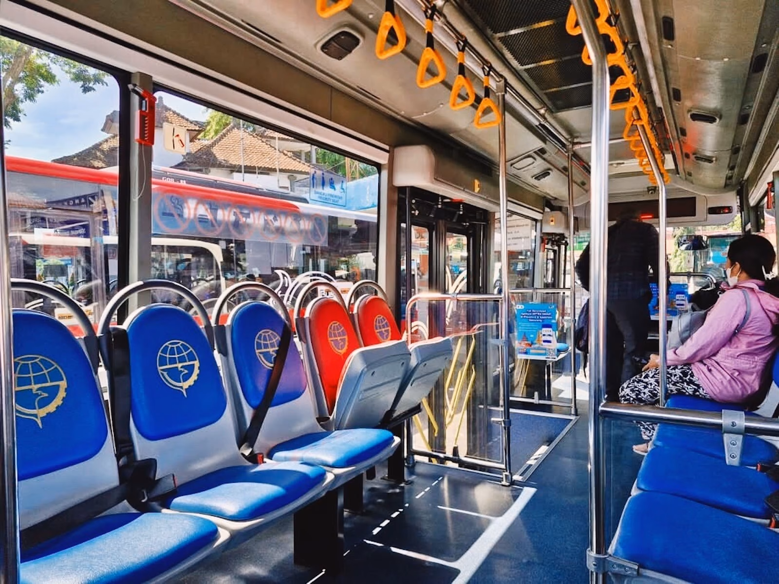 Trans Metro Dewata interior with blue and red seats, a central aisle and overhead handholds