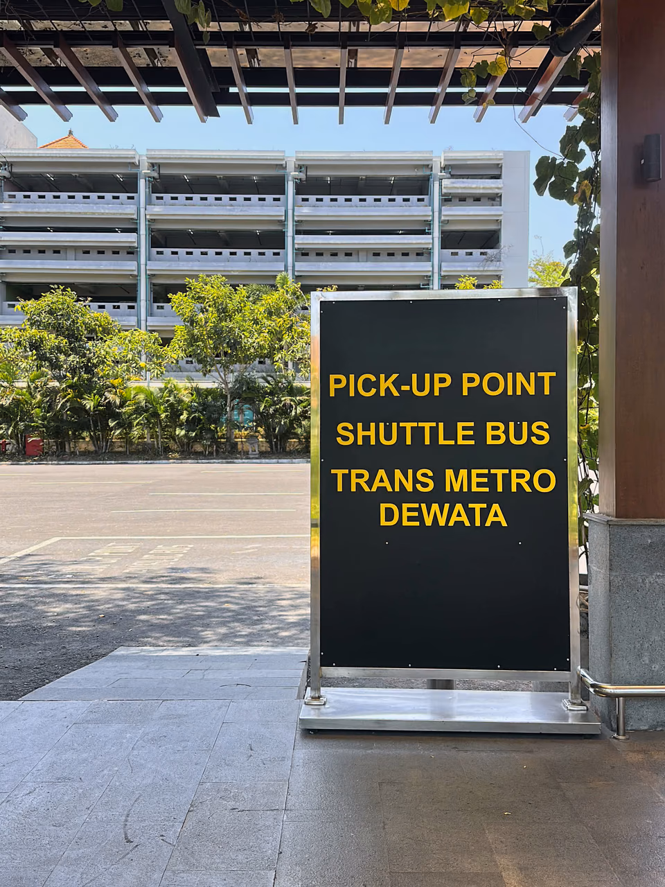 Sign reading Pick-up Point Shuttle Bus Trans Metro Dewata beside the terminal road