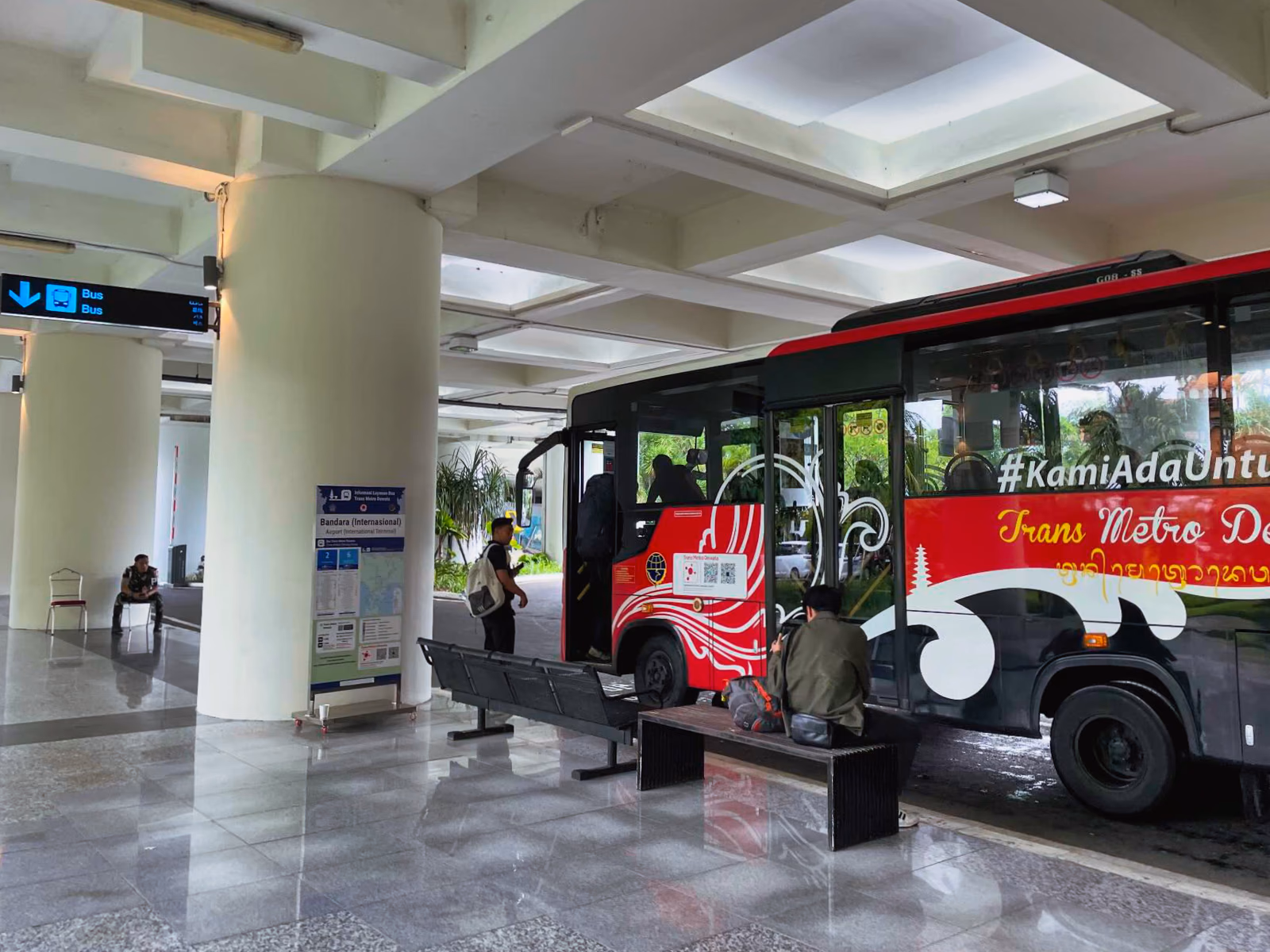 Trans Metro Dewata bus beside benches and a Bandara International Terminal bus stop information board